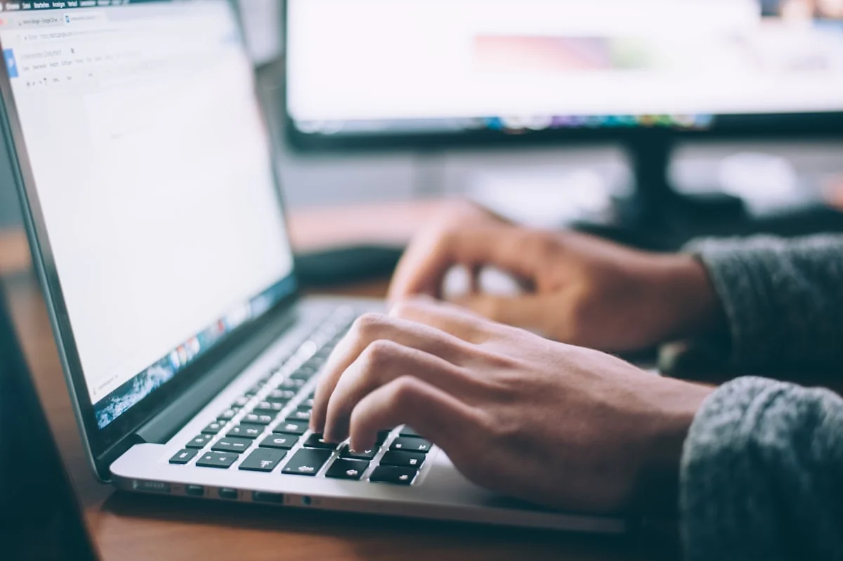 Persona escribiendo en un computador portátil mientras completa un formulario en línea