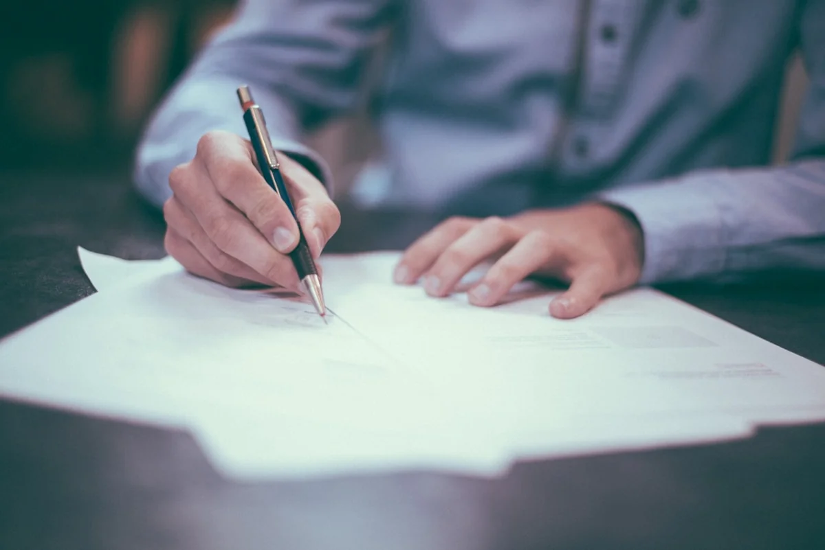 Persona firmando un documento sobre un escritorio con un bolígrafo