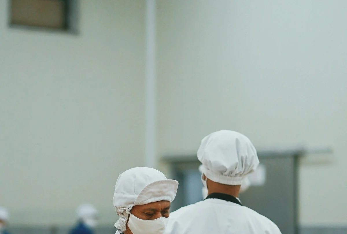 Trabajadores con delantal, cofia y mascarilla en una planta de procesamiento de alimentos